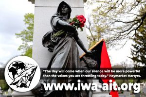 Mahnmal für die Opfer des Haymarket-Massakers von 1886 in Chicago, bestehend aus Steinsäule und weiblicher* Bronzefigur, die mit einem Blumenstrauß und einer rot-schwarzen Fahne geschmükt wurde